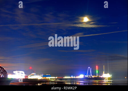 Moon and star trails at low tide over a brightly lit South Pier during Blackpool illuminations