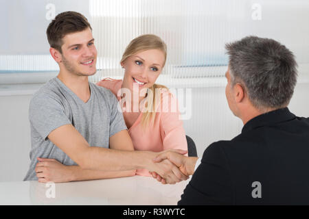 Couple Shaking Hands With Male Agent Stock Photo