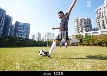 young asian soccer football player shooting the ball during match Stock Photo
