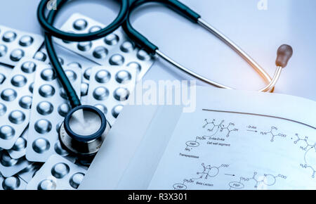 Pile of tablets pill in blister pack with drug structure book and stethoscope on white background. Medical equipment for diagnosis. Pharmacology textb Stock Photo