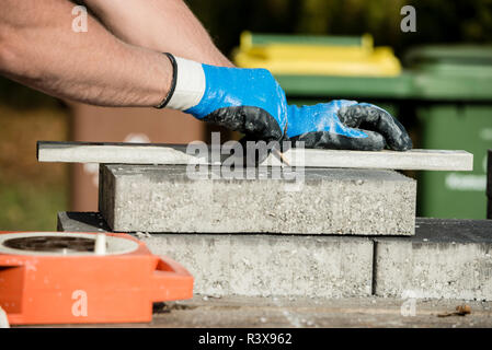 Builder marking a paving stone or block for cutting as he lays a new floor in a close up view of his gloved hands. Stock Photo