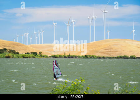 USA, California, Rio Vista, Sacramento River Delta. Sailboarder with turbines of wind farm in background. Stock Photo
