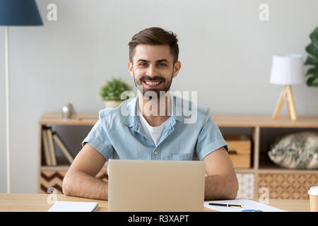 Portrait of happy male worker sitting at table using laptop Stock Photo