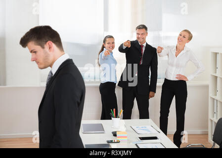 Businesspeople Teasing Businessman In Office Stock Photo