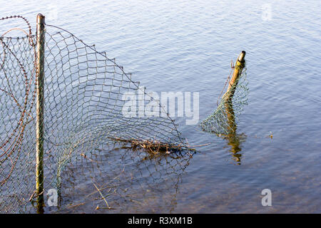 A chainlink fence reaching into the water. Auesee in Wesel, Germany Stock Photo