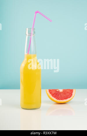 Orange drink and slice of grapefruit on white and blue background. Minimalistic image of citrus juice bottle and fruit at sparse bright environment. Stock Photo