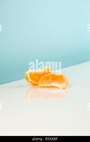 Wedges of tangerine on white table. Minimalistic image of piece of orange fruit on bright studio background Stock Photo