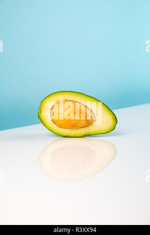 Half avocado fruit on white table. Minimalistic image of piece of alligator pear in bright studio background Stock Photo