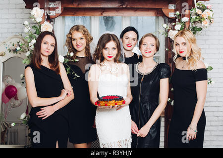 Beautiful bride-to-be with berry cake surronded by her bridesmaids in black dresses. Stock Photo