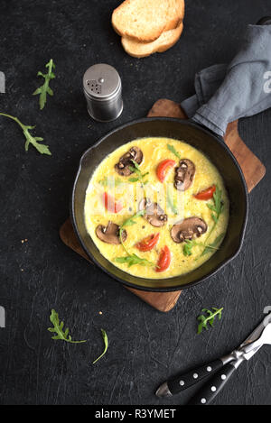 Omelette with mushrooms, tomatoes and arugula for breakfast on black background. Homemade omelette frittata, top view. Stock Photo