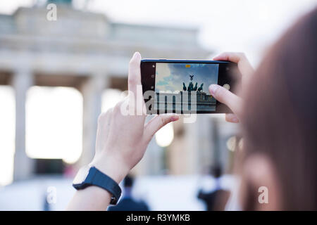 Hands holding phone mobile and takes pictures of famous historical tourist sites. The Brandenburg Gate neoclassical monument in Berlin. Stock Photo