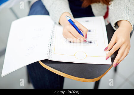 Crop hand of lady holding pen, writing in sketchbook and sitting at school desk Stock Photo