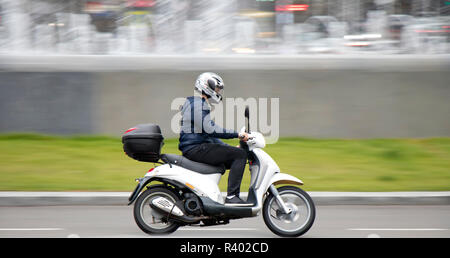 Belgrade, Serbia - July 19, 2018: One young man riding scooter with rear storage box on empty city street with fountain , panning shot Stock Photo