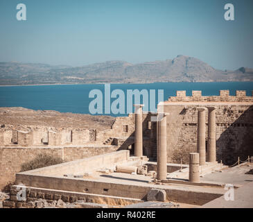 Horizontal photo with several pillars of Lindos Acropolis. Acropolys is on Rhodes island in Mediterranean Sea. Sea and sky is blue. Few rocks and hill Stock Photo