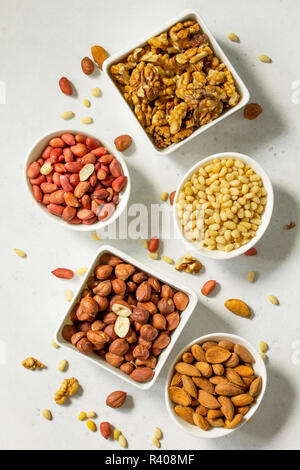 Various nuts in a ceramic bowl (walnut, almonds, pine nuts, hazelnuts) on a light stone table. The concept of a healthy dessert. Stock Photo