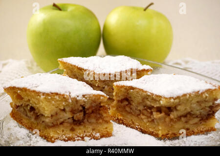Natural ingredients in home bakery. Three pieces of homemade traditional apple cake with two organic green apples in a background Stock Photo