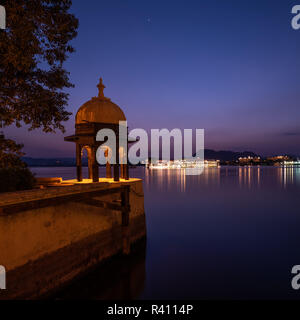 An ornate Chhatri or Canopy typical of Rajasthani architecture at night with Lake Pichola in the background. Stock Photo