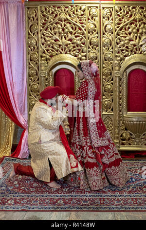 A Sikh bride and groom pose for their wedding photographer in a temple after their wedding ceremony. In Queens, New York City. Stock Photo