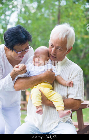 Asian crying baby comforted by grandparents at outdoor garden Stock Photo