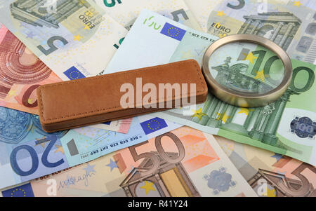 Magnifying glass lying on Euro banknotes, closeup, shallow DOF Stock Photo