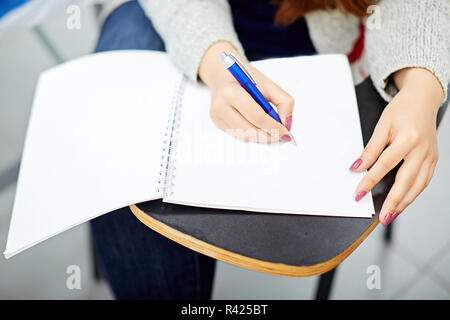 Woman writing in notebook and sitting on student table  Stock Photo