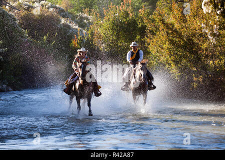 Usa, Wyoming, Shell, The Hideout Ranch, Cowboy and Cowgirl Riding Horses in the River (MR, PR) Stock Photo