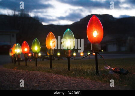 A row of Christmas lights sits in a front yard lawn with houses, a mountain and a night sky in the background. Stock Photo