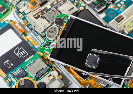 electronic chip in tweezers on background of the disassembled mobile phone Stock Photo