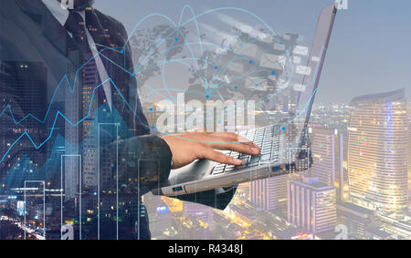 Double exposure of businessman using the laptop computer with cityscape and financial graph and network line on blurred building background, Business  Stock Photo