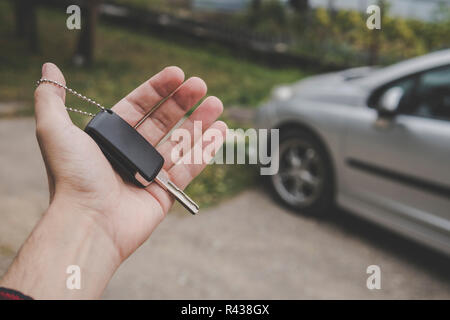 Close up of man's palm holding car key on a parked car background. Driver holds the vehicular key on the way to the vehicle. Man invites to have a dri Stock Photo