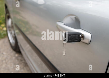 Inserted key in the car door outdoors. Close up of a carbody with the key left in the lock. Unlocking the vehicle doors. Opening motor before moving.  Stock Photo