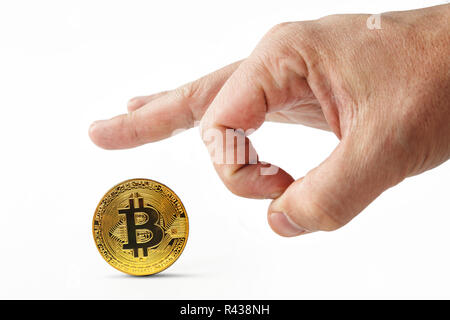 Male fingers push golden bitcoin away on a white background. Isolated man's hand throwing worthless cryptocoin away. Crash of cryptocurrency. Virtual money is depreciated. Useless bitcoins are kicked. Stock Photo