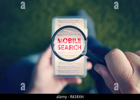 Top-down view of a sitting man with the magnifying glass with written red words Mobile Search above the smartphone screen. Man uses cell phone to browse search engine. Concept of mobile searching Stock Photo