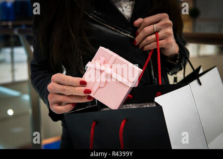 closeup of the hand of a young caucasian woman with her fingernails painted red holding a black shopping bag of gifts. Buying gifts for the new year and Christmas at the Mall. Stock Photo