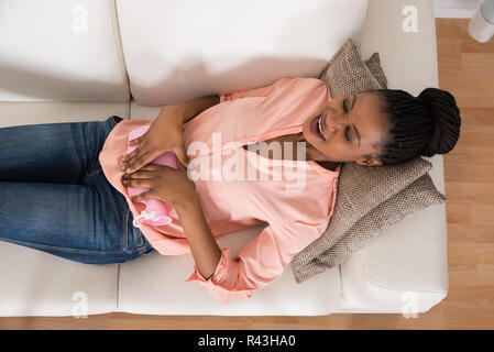 Woman Lying On Sofa With Hot Water Bag Stock Photo