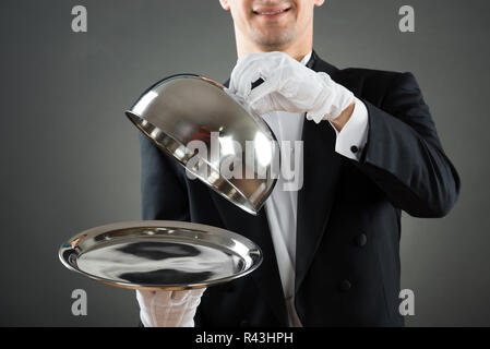 Midsection Of Waiter Holding Cloche Over Empty Tray Stock Photo
