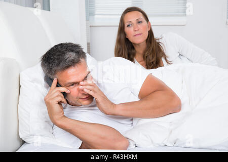 Woman Looking At Man Talking On Mobile Phone Stock Photo