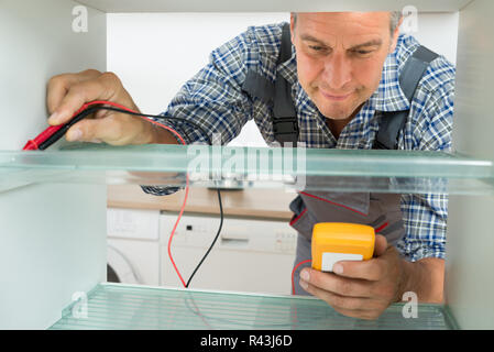 Repairman Checking Fridge With Digital Multimeter Stock Photo