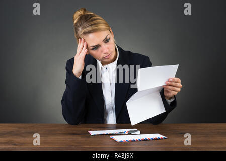 Shocked Businesswoman Reading Letter At Desk Stock Photo