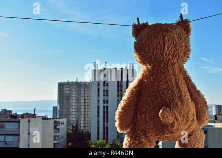 Cute brown Teddy Bear toy hanging on a clothesline with high building view Stock Photo