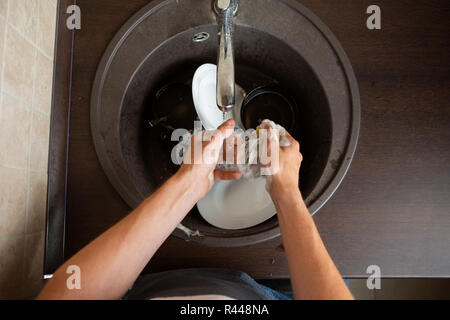 Picture from above of man's hands washing dish into sink Stock Photo
