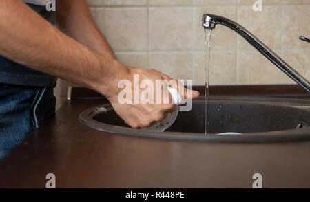 Photo of side of man's hands washing transparent mug in sink Stock Photo