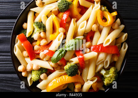 Italian penne pasta with chickpeas, vegetables, herbs and spices close-up in a plate on the table. Horizontal top view from above Stock Photo
