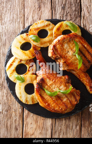 Freshly prepared delicious grilled pork chop in honey pineapple glaze close-up on slate on the table. Vertical top view from above Stock Photo
