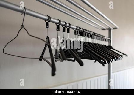 Close up shot of a row of black plastic coat hangers hung on metal tubes against a cream colour wall. First hanger is different than the rest. Stock Photo