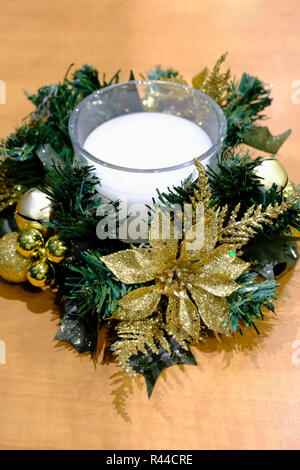 Christmas table decoration. White candle in glass surrounded by gold baubles and glitter flowers. Stock Photo