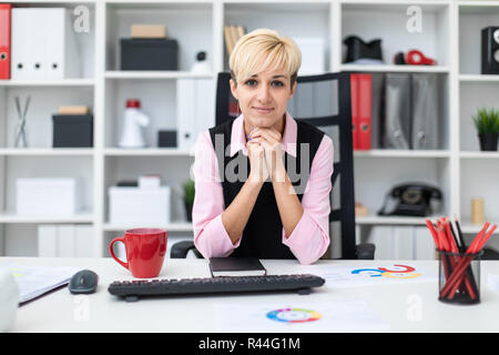A young girl works in a bright office with documents and a computer. The girl has short white hair. She's wearing a pink shirt and a black tank top. B Stock Photo