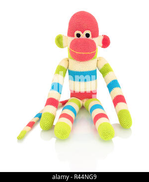 Cute handmade crochet monkey doll isolated on white background with shadow reflection. Playful crochet green pink blue white monkey sitting on white u Stock Photo