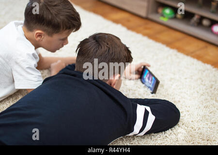 Little boys watching video by smartphone on carpet at home, rear view Stock Photo