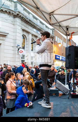 Young teenage man, signer, songwriter, Robbie White, on stage at open air show in Ramsgate town centre for the yearly turning on of the Christmas lights. Wears white hoodie and holding microphone singing to audience. Stock Photo